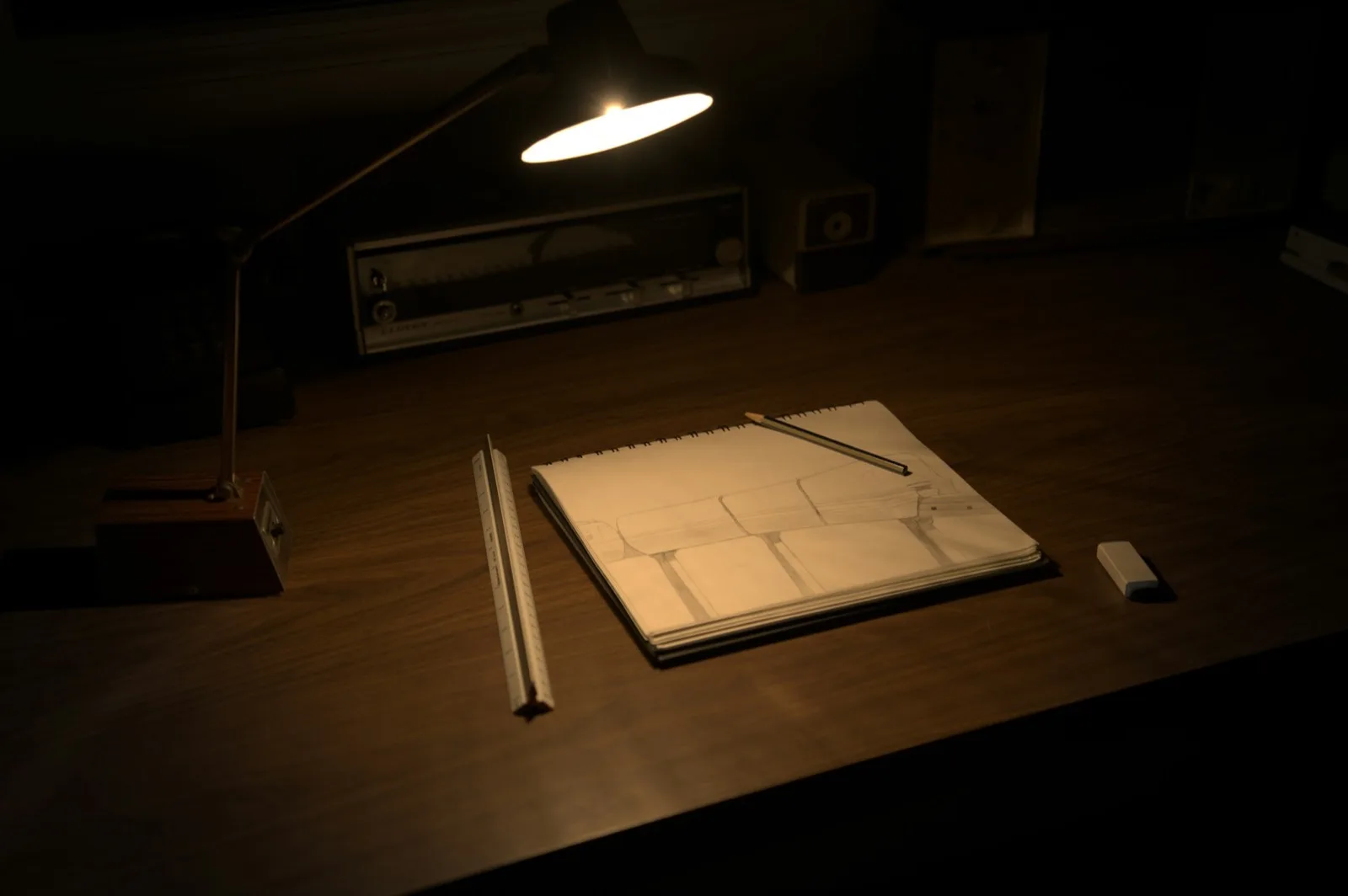 Uma mesa com um caderno de desenho, lápis e uma borracha sob um abajur