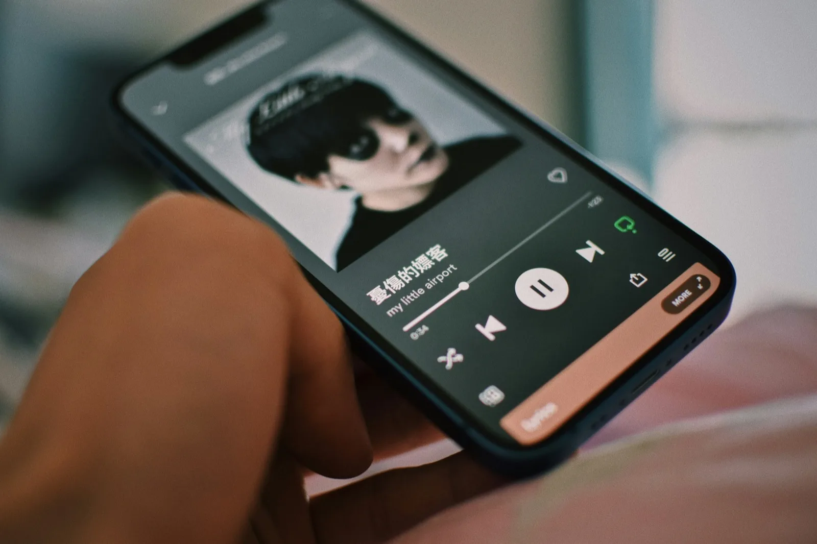 A hand holding a phone with a music player open on the screen